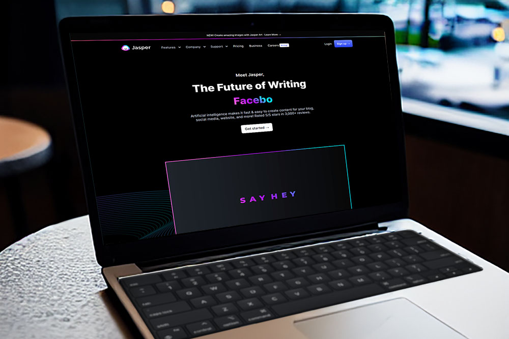 Laptop in a cafe with the homepage of Jasper AI showing